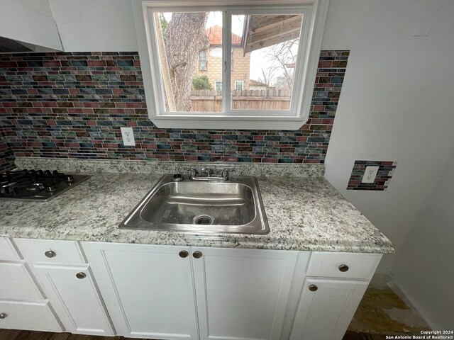 kitchen with decorative backsplash, white cabinets, light stone countertops, and sink