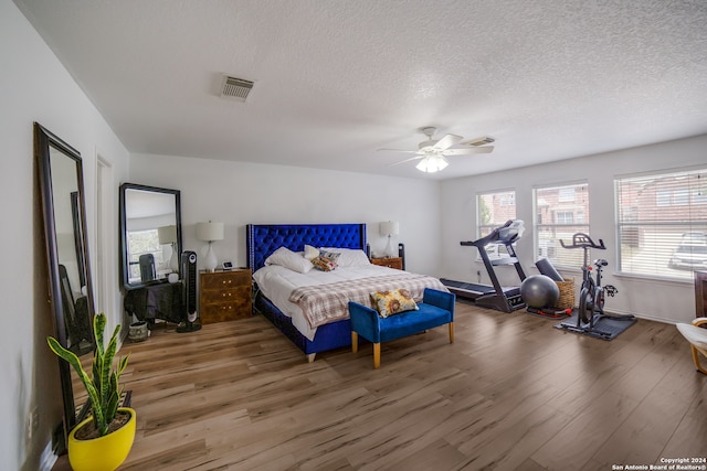 bedroom with a textured ceiling, wood-type flooring, and ceiling fan