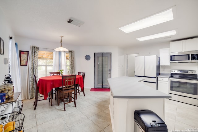 kitchen with appliances with stainless steel finishes, hanging light fixtures, white cabinetry, and light tile patterned floors