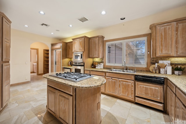 kitchen featuring sink, tasteful backsplash, stainless steel appliances, a center island, and light stone countertops