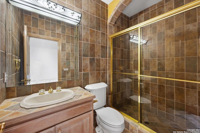 bathroom with tile walls, a shower with door, vanity, and toilet