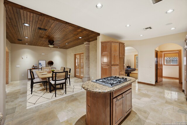 kitchen with wood ceiling, stainless steel gas cooktop, light stone countertops, a center island, and ceiling fan