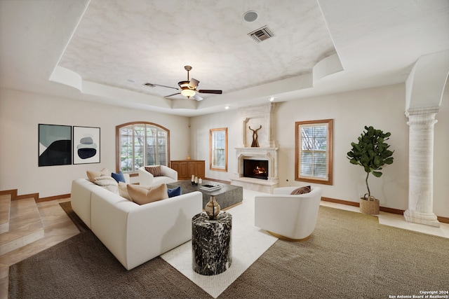 carpeted living room featuring ceiling fan, a tray ceiling, and ornate columns