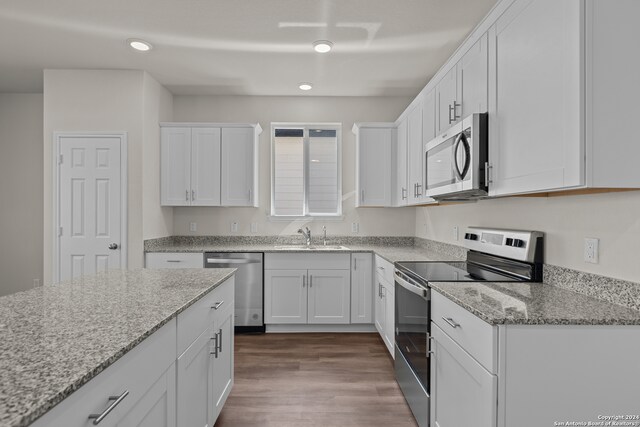 kitchen with white cabinets, light stone counters, appliances with stainless steel finishes, and hardwood / wood-style flooring