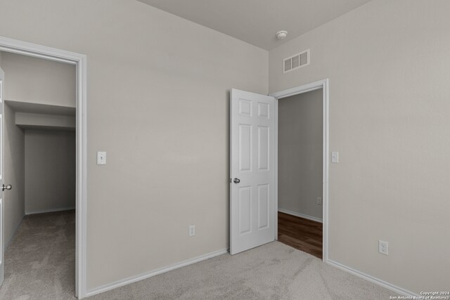 unfurnished bedroom featuring a walk in closet and light colored carpet