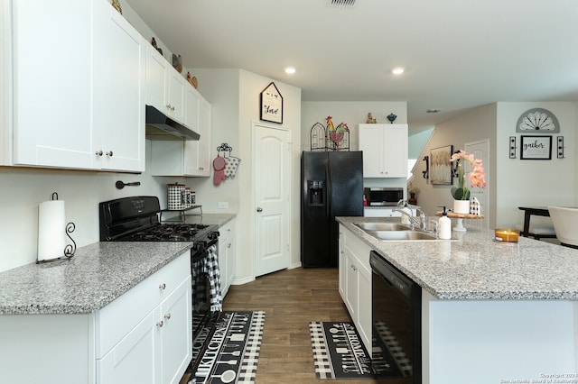 kitchen featuring light stone counters, white cabinets, a center island with sink, black appliances, and dark hardwood / wood-style flooring