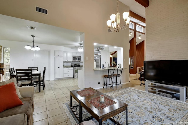 tiled living room featuring ceiling fan with notable chandelier, beam ceiling, sink, and high vaulted ceiling