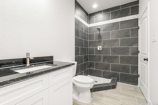 bathroom featuring a tile shower, vanity, and toilet