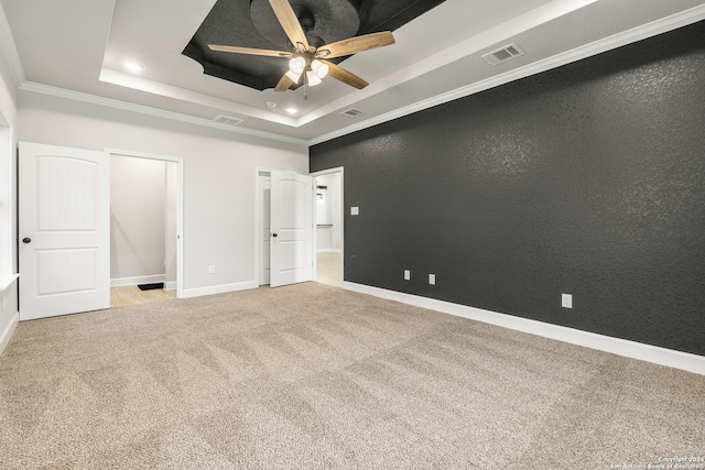 unfurnished bedroom with ceiling fan, light colored carpet, a tray ceiling, and crown molding