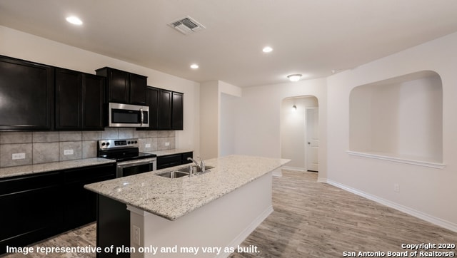 kitchen featuring decorative backsplash, stainless steel appliances, light hardwood / wood-style flooring, a center island with sink, and sink