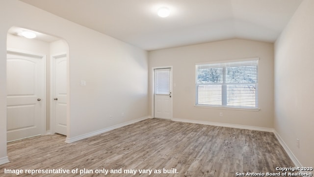 spare room with light wood-type flooring and lofted ceiling