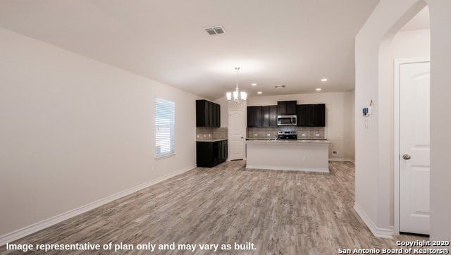 unfurnished living room featuring an inviting chandelier and light hardwood / wood-style flooring