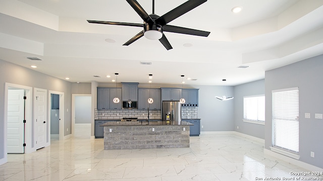 kitchen featuring appliances with stainless steel finishes, backsplash, ceiling fan, decorative light fixtures, and a kitchen island with sink