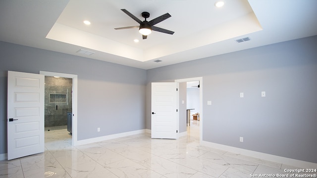 unfurnished bedroom featuring connected bathroom, ceiling fan, and a tray ceiling