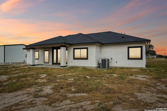 back of house featuring stucco siding, a shingled roof, and central AC