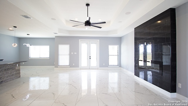 empty room featuring french doors, a tray ceiling, a healthy amount of sunlight, and ceiling fan