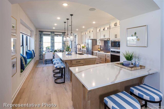 kitchen with appliances with stainless steel finishes, a large island with sink, pendant lighting, sink, and white cabinetry