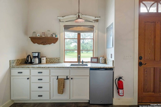 kitchen with light stone counters, pendant lighting, sink, stainless steel dishwasher, and white cabinetry