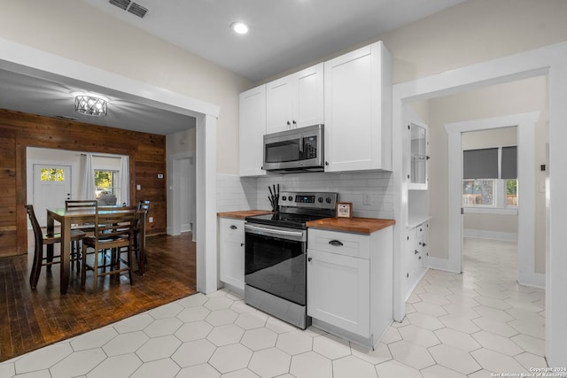 kitchen featuring white cabinets, wooden walls, stainless steel appliances, and wooden counters