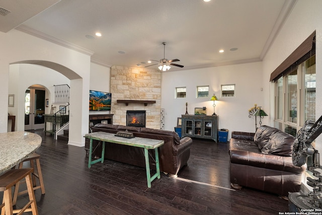 living room featuring ceiling fan, crown molding, dark wood-type flooring, and a stone fireplace