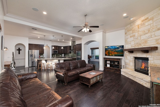 living room with a textured ceiling, a fireplace, dark hardwood / wood-style flooring, ornamental molding, and ceiling fan