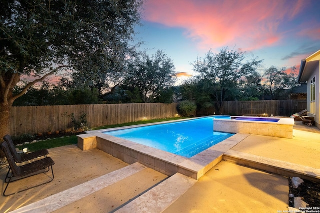 pool at dusk with a patio and an in ground hot tub