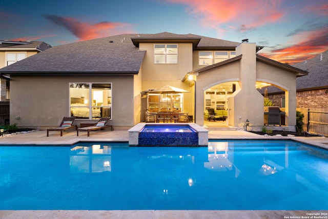 pool at dusk featuring a patio and an in ground hot tub