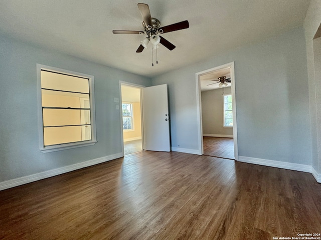 unfurnished bedroom featuring multiple windows, dark hardwood / wood-style floors, and ceiling fan