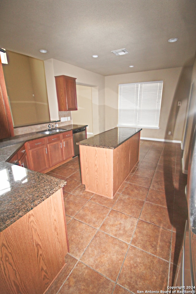 kitchen featuring sink, a kitchen island, dishwasher, dark stone countertops, and tile patterned flooring