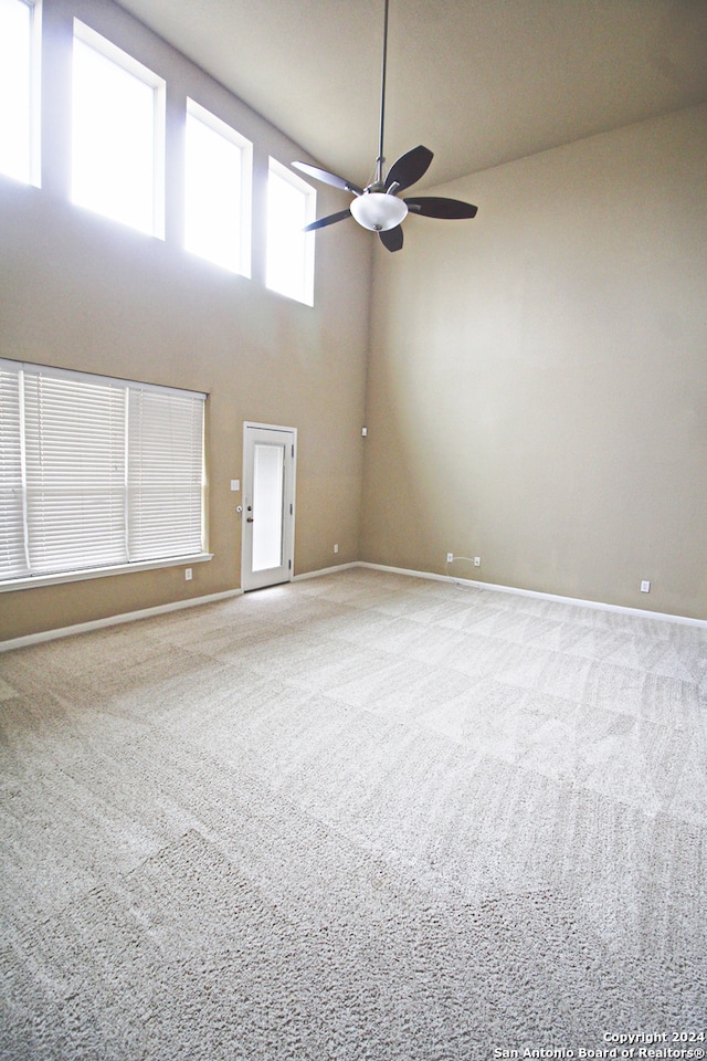 carpeted spare room with a towering ceiling and ceiling fan