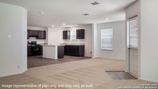 kitchen featuring dark brown cabinetry, sink, a center island, light carpet, and black stove