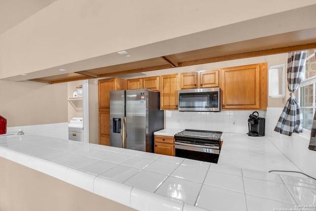 kitchen featuring stainless steel appliances, washer / clothes dryer, kitchen peninsula, and tile countertops