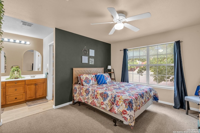 bedroom with ensuite bath, ceiling fan, light colored carpet, and sink