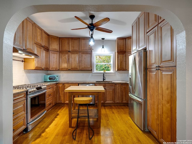 kitchen with appliances with stainless steel finishes, decorative backsplash, ceiling fan, light hardwood / wood-style flooring, and sink