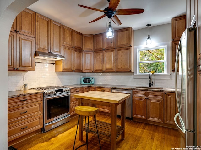 kitchen with light stone counters, hardwood / wood-style flooring, sink, stainless steel appliances, and ceiling fan