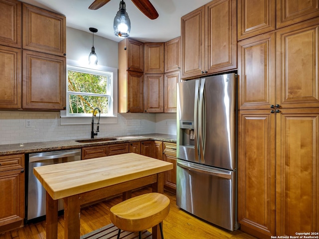 kitchen featuring light stone counters, hanging light fixtures, sink, stainless steel appliances, and light wood-type flooring