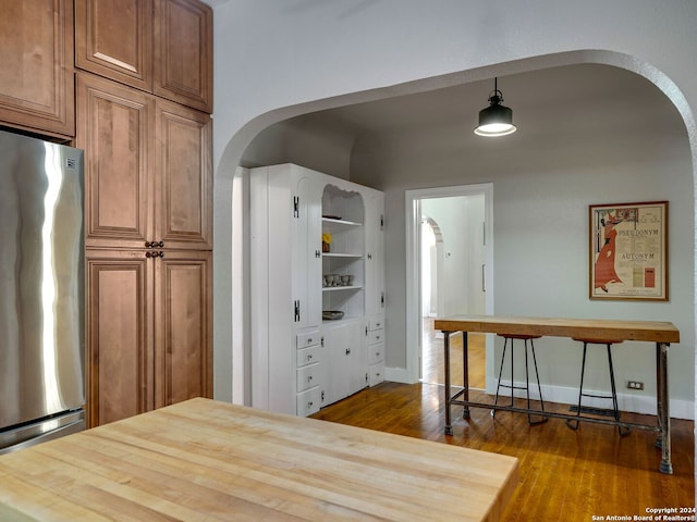 kitchen with hanging light fixtures, hardwood / wood-style floors, stainless steel fridge, and wooden counters