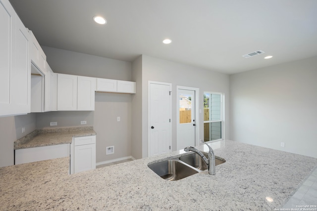 kitchen featuring light stone countertops, white cabinets, and sink