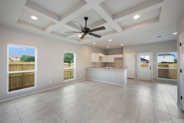 unfurnished living room with ceiling fan, beamed ceiling, coffered ceiling, and a healthy amount of sunlight