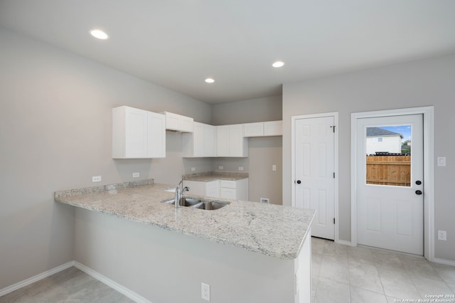 kitchen featuring light stone counters, light tile patterned floors, sink, kitchen peninsula, and white cabinetry