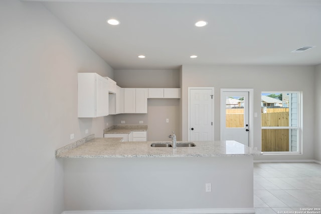 kitchen featuring light stone counters, white cabinets, light tile patterned floors, sink, and kitchen peninsula