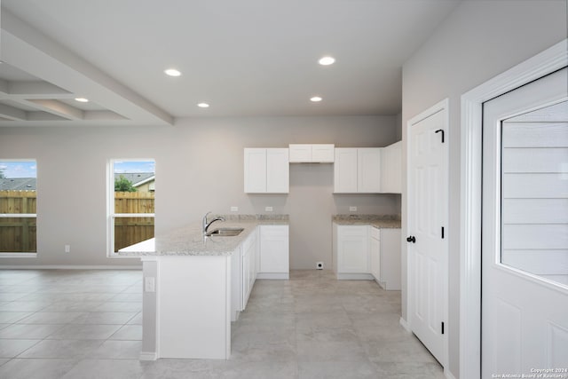 kitchen featuring white cabinetry, light stone counters, light tile patterned floors, beam ceiling, and sink