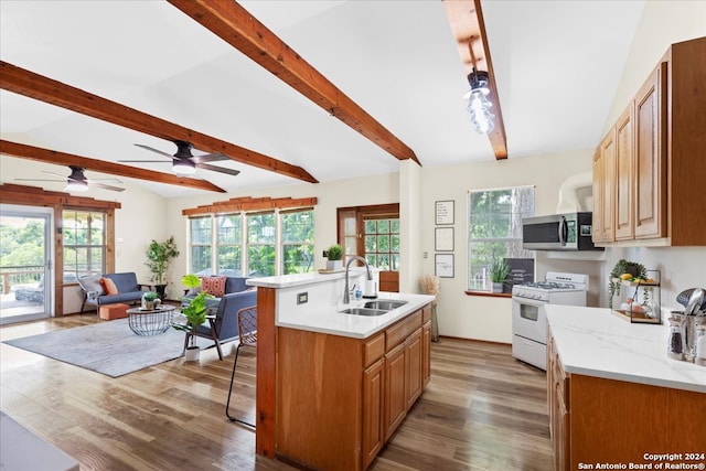 kitchen featuring lofted ceiling with beams, gas range gas stove, light hardwood / wood-style flooring, a center island with sink, and sink