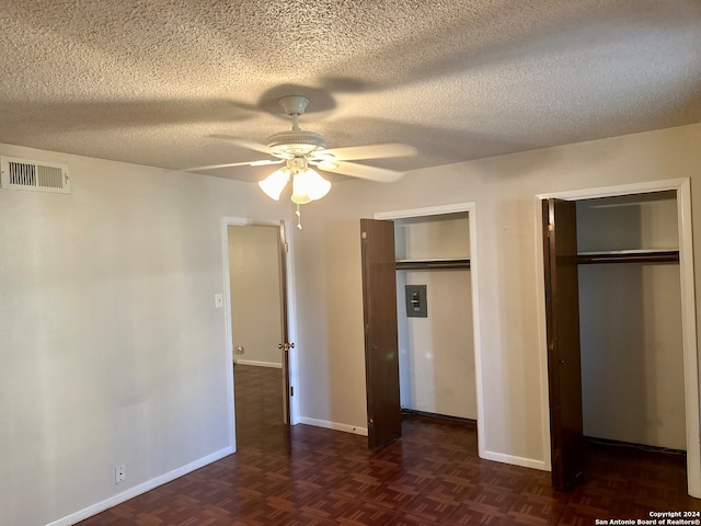 unfurnished bedroom featuring a textured ceiling, dark parquet floors, ceiling fan, and multiple closets