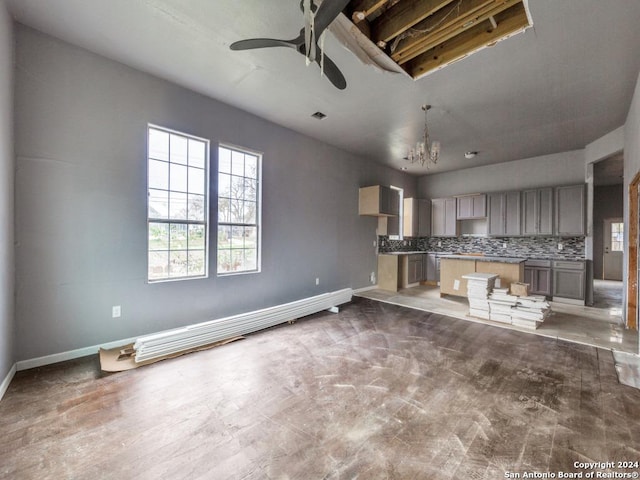 unfurnished living room with ceiling fan with notable chandelier, baseboards, and a healthy amount of sunlight