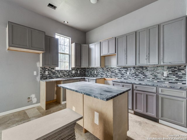 kitchen with visible vents, baseboards, gray cabinets, backsplash, and a kitchen island