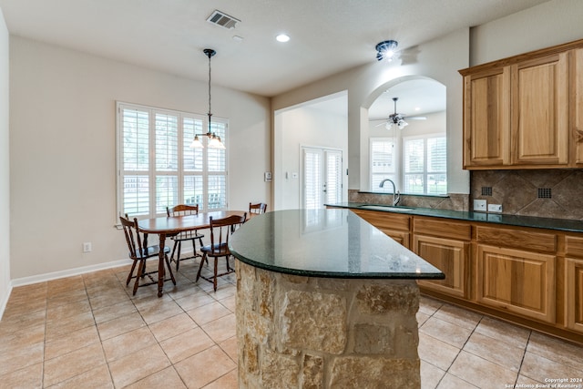 kitchen featuring decorative backsplash, light tile patterned flooring, ceiling fan with notable chandelier, a kitchen island, and sink