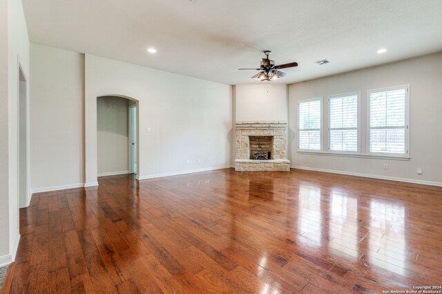 unfurnished living room featuring ceiling fan, a stone fireplace, and hardwood / wood-style floors