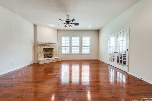 unfurnished living room with a fireplace, dark wood-type flooring, ceiling fan, and french doors