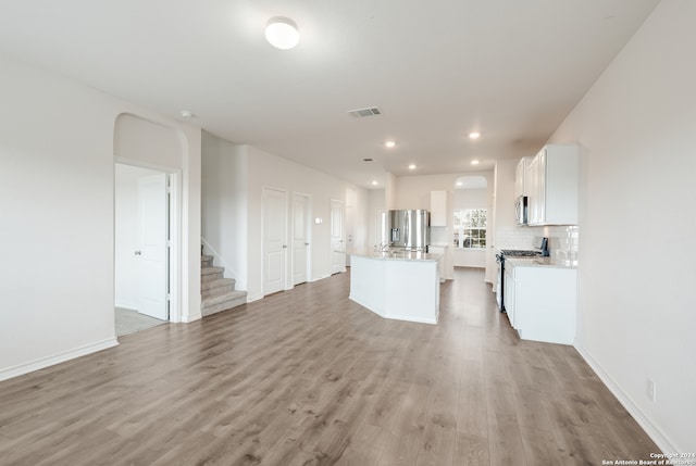 kitchen featuring backsplash, white cabinetry, stainless steel appliances, a center island, and light hardwood / wood-style floors